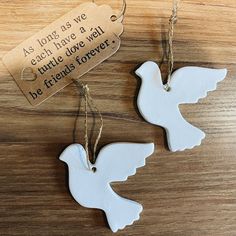 two white doves hanging from twine on a wooden table with a tag that says as long as we each have a true love well be friends forever