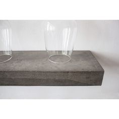 two clear glass vases sitting on top of a cement block in front of a white wall