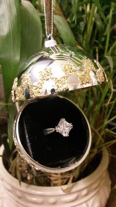 a diamond ring sits in an open box on top of a plant with green leaves