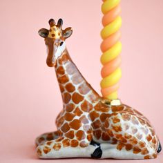 a giraffe laying down next to a yellow and orange toy on a pink background