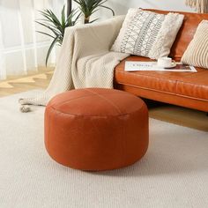 a living room with an orange leather couch and ottoman in the corner, next to a potted plant