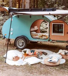 an outdoor food trailer is set up in the woods with picnic blankets and baskets on the ground