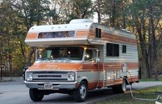 an orange and white motor home parked on the side of a road next to trees