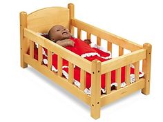 a baby doll laying in a wooden crib with a red blanket on it's back