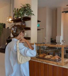 a woman standing in front of a bakery counter looking at pastries on display behind the counter