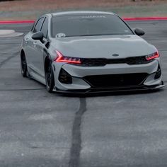 the front end of a white car driving on a race track with red lines in the background