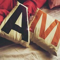 two pillows sitting on top of a bed next to each other with the letter a on them