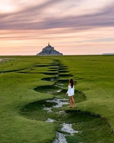 a woman in white dress walking across a field with a castle in the back ground