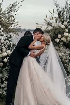 a bride and groom kissing in front of an arch with flowers on the side at their wedding