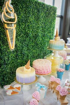 a table topped with cakes and desserts next to a tall green wall covered in greenery