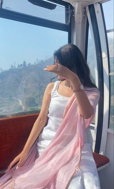 a woman sitting on top of a bus next to a window with mountains in the background