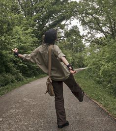 a person walking down a dirt road with trees in the background and one arm outstretched