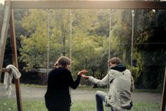 two people sitting on swings in a park, one holding the other's hand