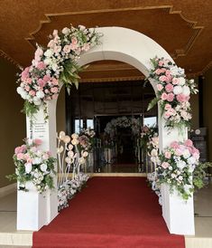 an archway decorated with flowers and greenery at the end of a red carpeted walkway