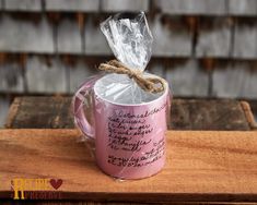 a pink coffee mug with a message wrapped in cellophane sitting on top of a wooden table