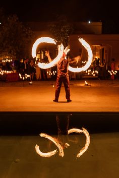 a man standing in front of a body of water holding two circular fire hoopes