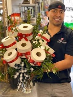 a man holding a bunch of toilet paper wrapped in red and white ribbon with greenery