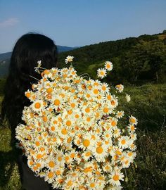 a woman holding a bouquet of daisies in her hands on top of a hill