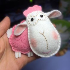 a hand holding a pink and white sheep brooch on it's left side