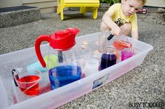 a toddler playing in a plastic container filled with water and liquid while pouring station