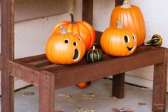 three pumpkins with faces painted on them sitting on a bench