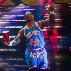 a man in a blue basketball uniform holding a red cup and wearing sunglasses on stage