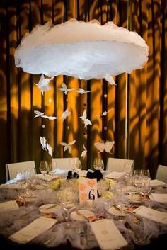 the table is set with white linens and paper butterflies hanging from it's centerpiece