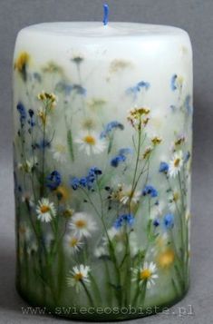 a white candle with blue and yellow flowers painted on the front, sitting on a gray surface