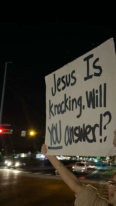 a woman holding up a sign that says jesus is knocking, will you answer?