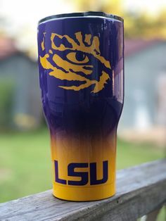 a purple and yellow tumbler sitting on top of a wooden fence