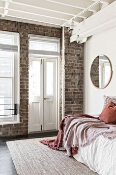 a bedroom with brick walls and white bedding in front of a mirror on the wall