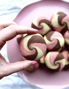 a pink plate filled with brown and white swirly cookies on top of a table