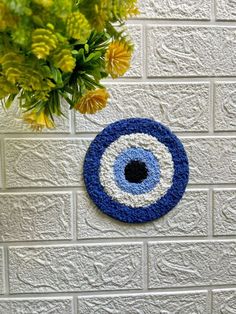 a blue and white crocheted eyeball hanging on a brick wall next to flowers