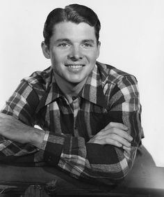 an old black and white photo of a young man with his arms crossed sitting at a table