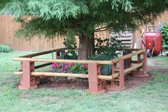 a wooden bench sitting next to a tree in a yard with pink flowers on the ground