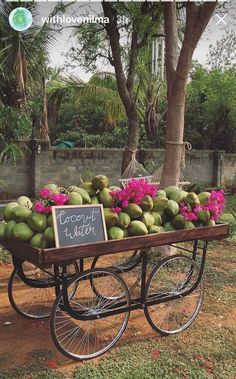 a cart filled with coconuts and pink flowers in front of a tree on the side of a road