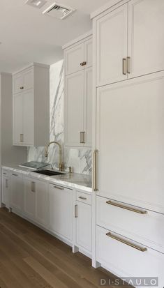 a kitchen with white cabinets and marble counter tops, gold handles on the faucets