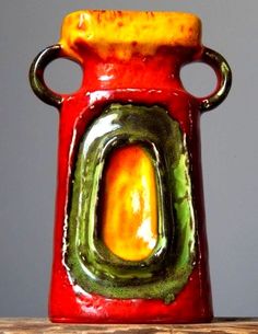 a red vase sitting on top of a wooden table covered in green and yellow decorations