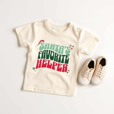 "Kids will look adorable in this \"SANTA'S FAVORITE HELPER\" youth short sleeve tee. This lightweight side-seamed shirt maximizes comfort all day long.  Santa's Favorite Helper Kids Toddler Youth, Christmas T Shirt, Santa Shirts for Kids, Boy Kids Holiday Outfit Holiday Shirts 🌟100% Airlume combed and ringspun cotton (fiber content may vary for different colors) 🌟Light fabric (3.9 oz/yd² (132 g/m 🌟Retail fit RETURNS: All products are made-to-order and because of the nature of these items, all White Short Sleeve Christmas Shirt, Cute Short Sleeve T-shirt For Winter, Festive Short Sleeve Shirt With Letter Print, Family Matching Short Sleeve Holiday Shirt, Cute Holiday Tops With Short Sleeves, Cute Short Sleeve Holiday Tops, Pre-shrunk Short Sleeve Christmas Tops, Cute Christmas T-shirt With Letter Print, Christmas Cotton Short Sleeve Shirt