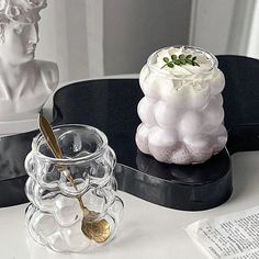 two glass vases sitting on top of a black table next to a white busturine