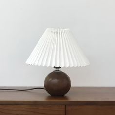 a lamp sitting on top of a wooden table next to a white wall and dresser