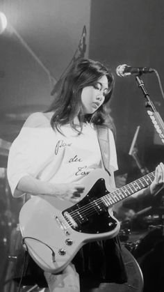 black and white photograph of a woman playing guitar on stage with microphone in the background