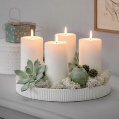 three white candles with succulents and green leaves on a tray in front of a mirror