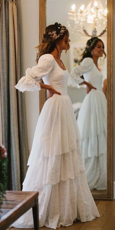 a woman in a white wedding dress looking at herself in the mirror with her hands on her hips