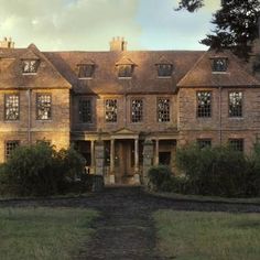 an old brick building with lots of windows on the front and side of it, surrounded by green grass