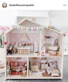 a doll house with lots of furniture and decorations on the top floor, in front of pink tulips