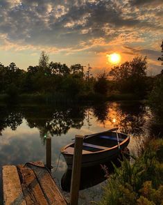 a small boat sitting on top of a lake next to a wooden dock at sunset