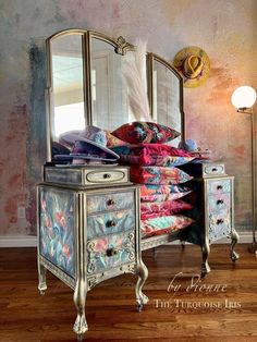 an ornate dresser and mirror in front of a colorful wallpapered room with wood flooring