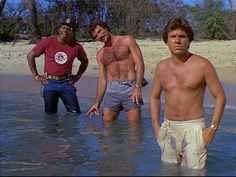 three men are standing in the water at the beach and one is not wearing a shirt