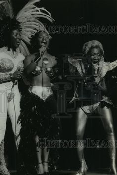 vintage black and white photograph of three women in costumes singing on stage with one holding a microphone